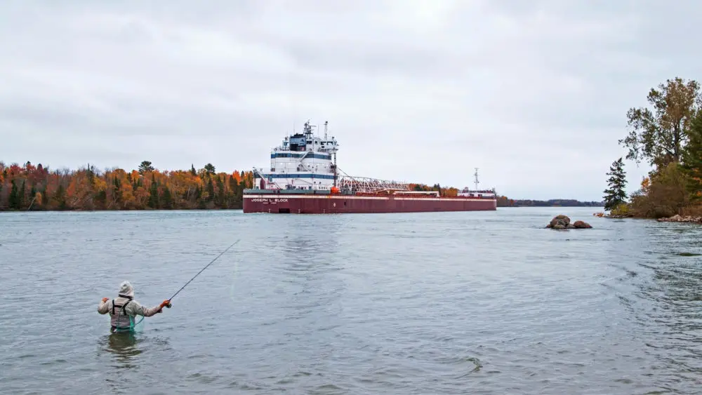 Man fly fishing at Rotary Park as a freighter passes by